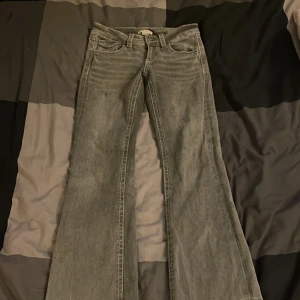 Grå bootcut jeans från Gina Tricot - Snygga grå jeans från Gina Tricot i storlek 152. Modellen har bootcut-ben och klassisk femficksdesign med knappdetalj på bakfickan. Jeansen är tillverkade i ett mjukt denimtyg och har låg midja för en trendig look.