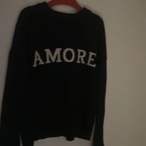 Svart stickad tröja AMORE Gina Tricot - Svart stickad tröja från Gina Tricot med vit text 'AMORE' framtill. Klassisk rund halsringning och långa ärmar. Perfekt för dig som vill ha en enkel men ändå statement tröja till hösten eller vintern.