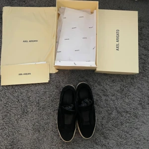 Axel arigato Laceless skor - Svarta sneakers från Axel Arigato med stilren design och vit platt sula. Skorna är i mocka och utan snören. Perfekta för dig som gillar en clean och modern stil. Allt på bilden medföljer. Ps är inte hugget i sten. Ny pris 2300