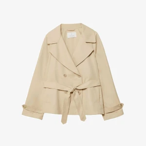 Beige trenchcoat med bälte från Stradivarius  - Snygg kort trenchcoat i beige med klassisk krage, dubbelknäppning och bälte i midjan. Jackan har långa ärmar med knappar vid ärmslut och en avslappnad passform. Perfekt för dig som vill ha en stilren och trendig look.