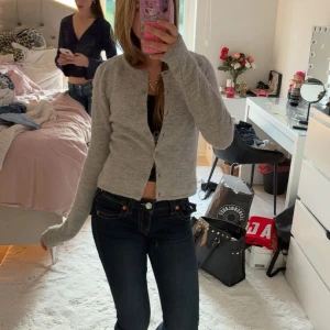 Grå kofta med knappar från Gina  - Mysig ljusgrå kofta från gina med rund halsringning och knäppning framtill. Koftan är stickad i mjukt material och har långa ärmar. Perfekt att slänga över en topp för en chill look.