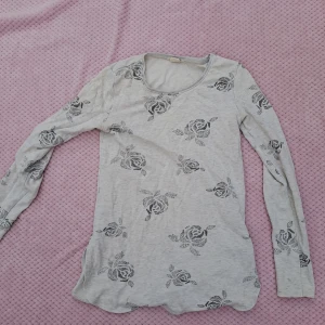 Ljusgrå långärmad tröja med rosor - Ljusgrå långärmad tröja med svart blommigt rosmönster över hela. Tröjan har rund halsringning. Den har roliga små slits på sidan! Den har barnstorlek men som en xs-s passar den mig bra