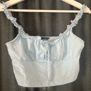 Ljusblå croppad linnetopp från SHEIN - Supersöt ljusblå croppad linnetopp från SHEIN med volangprydda axelband och knytning framtill. Toppen har en enkel, rak passform och är tillverkad i mjuk bomullsmix. Perfekt för varma dagar när du vill ha en söt och chill look.