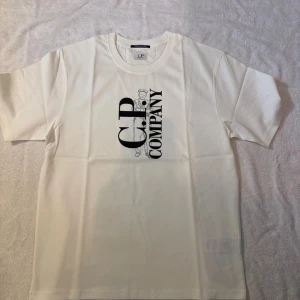 Vit C.P. Company t-shirt Metropolis - Vit Tisha från C.P. Company, mer exakt deras linje ”Metropolis”. Schysst print på framsidan med loggan men tom på ryggen. Helt nytt skick och skickar med cp påsen. Storleken är M och passformen syns i bilden, grabben är 179 65kg. Skicka bud