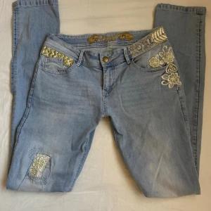 Ljusblå broderade jeans från Desigual - Ljusblå jeans från Desigual med broderade blommor i silver och guld vid fickorna och på benet. Strl 28.