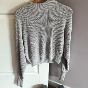 Ljusgrå stickad tröja från NA-KD - Säljer en ljusgrå stickad tröja från NA-KD i storlek XS. Tröjan har en ribbad struktur, hög krage och långa ärmar med breda muddar. Perfekt för lager-på-lager och chill dagar. Enkel att matcha med jeans eller kjol.