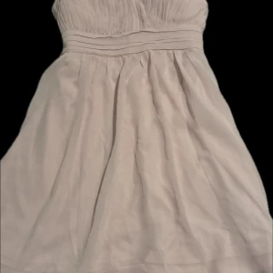 Ljusrosa axelbandslös klänning Model Behaviour - Supersöt ljusrosa axelbandslös klänning från Model Behaviour. Klänningen har plisserad överdel, markerad midja och ett lätt, flowy tyg som ger en romantisk känsla. Perfekt för dig som vill ha en feminin och stilren look.