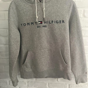 Grå hoodie från Tommy Hilfiger - Snygg grå hoodie från Tommy Hilfiger med broderad logga och text på bröstet. Säljer den då jag har bytat till en annan stil och det är storlek S 