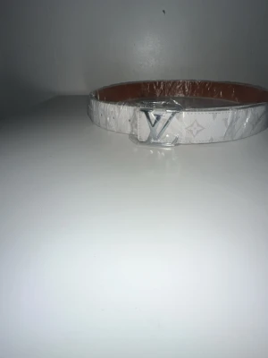  Louis Vuitto - Snyggt vitt bälte från Louis Vuitto i äkta läder med klassiskt L-monogram och silverfärgat Lspänne. Bältet har en stilren design och är tillverkat i Spanien. Perfekt accessoar för att lyfta din outfit.