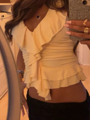 Gul volang topp med omlott - Snygg gul halterneck topp med volangdetaljer. Ärmlös modell med djup v-ringning och flera lager volanger framtill och nedtill. 🫶🏽