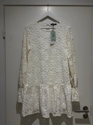 Vit spetsklänning med volang - Superfin vit kort spetsklänning från Gina Tricot med långärmade ärmar och volang nertill. Perfekt för dig som vill ha en söt och snygg studentklänning. Ej använd och prislappen kvar 