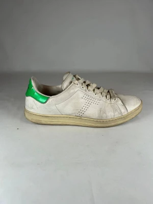 Tom Ford sneakers  - Tom Ford sneakers i vitt skinn med grön detalj på hälen. Modellen har snörning, perforerade ränder på sidan och platt sula. Perfekta för en stilren look. Förutom skrynklorna och hälen så är dem helt defekt fria, bara lite smutsiga som man enkelt kan tvätta.   Nypris på skorna är över 10 000 vilket gör detta till ett mycket rimligt pris utifrån defekterna och smutset.  Tveka inte på att ställa frågor!