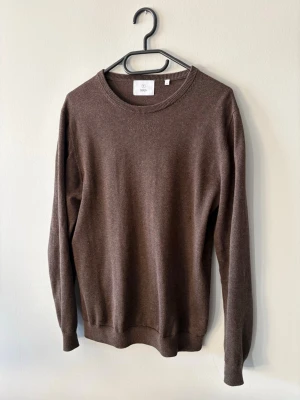Brun stickad tröja från Bläck - Mysig brun stickad tröja från Bläck i storlek S. Klassisk rund halsringning och långa ärmar. Perfekt till höst och vinter när du vill ha något enkelt men ändå stilrent. Liten skada vid sidan av magen men inget som syns.