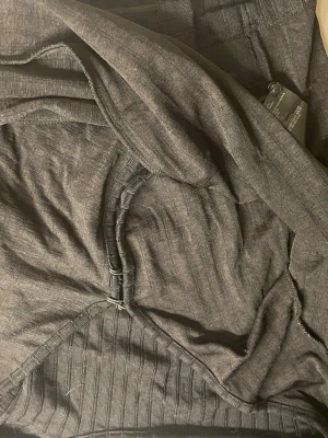 Mörkgrå ribbstickad kofta - Mörkgrå kofta med ribbstickade detaljer och dragkedja framtill. Koftan har lång ärm och är tillverkad i ett mjukt, tunt material som känns skönt mot huden. Perfekt för lager-på-lager och enkel att matcha med andra plagg.