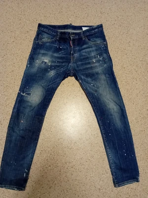 Dsquared2 jeans med röda och vita färg stänk. - Riktigt fina dsquared2 jeans som är stilrena och passar till det mesta! Jeansen är av högsta kvalité och har riktigt bra passform. Jeansen har några år på nacken men har används sällan och är fortfarande i bra skick. Jeansen är unika och det står "honey baby come inside xxx" ovanför högra ficka. Passa på att köpa dessa unika äkta dsq2 jeans! 