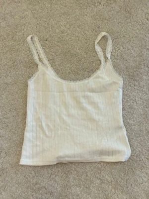 Vit ribbad spetslinne - Säljer ett vitt ribbat linne med tunna axelband och spetsdetaljer längs kanterna. Linnet har en mjuk, stretchig passform och är perfekt för sommardagar eller som lager under en skjorta. Materialet känns lätt och luftigt.