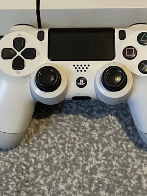 Vit PlayStation 4 med handkontroll - Säljer en vit PlayStation 4 med matchande vit DualShock 4-handkontroll. Konsolen har en stilren, rektangulär design och är tillverkad i plast. Perfekt för gaming med HDMI, nätverksport och USB-anslutningar på baksidan.