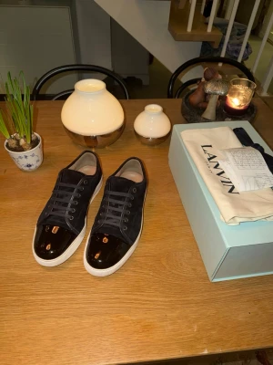 LANVIN skor  - Stilrena mörkblåa sneakers från Lanvin med vit sula och glansig tå i lack. Skorna har snörning och är tillverkade i mocka med detaljer i skinn. Perfekta för dig som vill ha en lyxig och modern look. Skick 9/10.