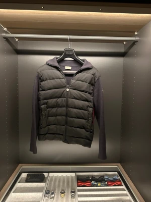 Moncler cardigan - Snygg mörk grå wool tricot cardigan från Moncler med quiltad front och stickade ärmar och rygg. Jackan har röda detaljer längs sidorna. Perfekt för lager på lager och ger en clean look. Storleken är M men passar S 