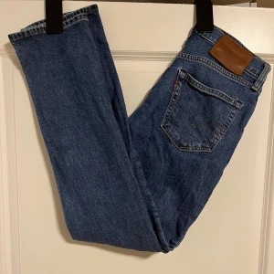 Levi's 511 blå jeans W28 L32 - Säljer ett par klassiska Levi's 511 jeans i mörkblå tvätt. Modellen har en slim passform med raka ben och fem fickor. Jeansen har den ikoniska bruna läderpatchen bak och är tillverkade i slitstarkt bomullsjeansmaterial. Perfekt för dig som gillar en tidlös look.