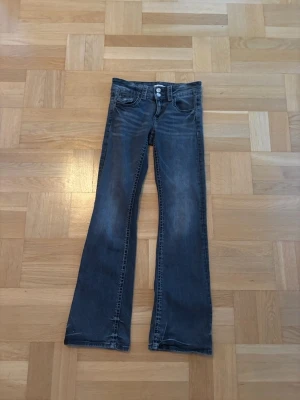Blå bootcut jeans med låg midja - Snygga blå jeans med bootcut passform och låg midja. Klassisk femficksmodell med slitningar framtill för en cool look. Tillverkade i mjukt denimtyg som sitter skönt hela dagen. 