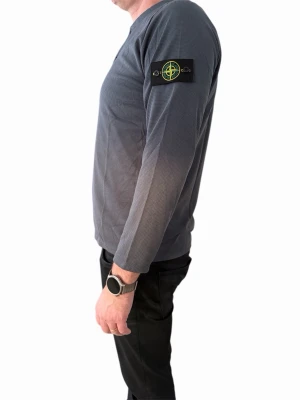 Grå långärmad tröja Stone Island - Säljer en grå långärmad tröja från Stone Island med klassisk patch på ärmen. Tröjan har knappar vid halsen och är tillverkad i ett strukturerat bomullstyg. Perfekt för dig som gillar stilrena och avslappnade plagg.