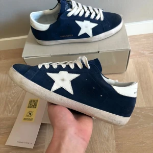Golden goose skor - Golden Goose Superstar sneakers i mörkblå mocka med vit stjärndetalj på sidan och vit hälkappa. Nyskick, endast lite smutsiga, använda vid max 10 tillfällen. Allt og ingår! Storlek 43.