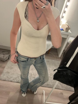 Ribbad cremefärgad topp med v-ringning - Snygg ribbad cremefärgad topp med djup v-ringning och breda axelband. Toppen är figurnära och har en stickad känsla som ger en trendig look. Perfekt att styla med jeans eller kjol för en cool vardagsstil.  Säljer denna jätte fina toppen då den aldrig kommit till användning men prislappen är tyvärr borttagen! ❤️ Från H&M i storlek XS, inga fläckar eller liknande. Djur och rökfritt hem! Skriv gärna om du har frågor. Pris kan diskuteras vid snabb köp!🙂