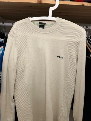 Beige tröja från BOSS - Snygg beige långärmad tröja från BOSS med diskret logga på bröstet. Tröjan har rund halsringning och ribbade detaljer på axlar och ärmar. Tillverkad i ett mjukt material med thermal comfort för extra värme. Perfekt för dig som gillar stilrena plagg. PRIS KAN DISKUTERAS!!!Nypris runt 800 kr och 