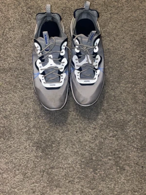 Nike React Element 87 grå/blå sneakers - Nike React Element 87 sneakers i grått med blå och vita detaljer. Snygg design med genomskinlig mesh, vita och blå accenter samt unik sula med reaktionsdämpning. Skorna har snörning och en sportig vibe som sticker ut. Ny pris 1700 kr,   Pris kan diskuteras 