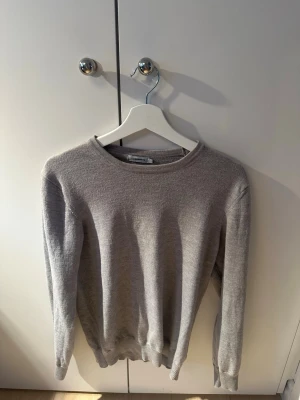 Ljusgrå stickad tröja J.Lindeberg - En stilren ljusgrå stickad tröja i 100% merino ull.