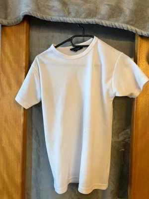 Vit t-shirt från No Problem XS - Klassisk vit t-shirt från No Problem i storlek XS. T-shirten har rund halsringning och korta ärmar, tillverkad i ett lätt och bekvämt material som passar perfekt till vardags. Enkel och stilren design som funkar till det mesta.