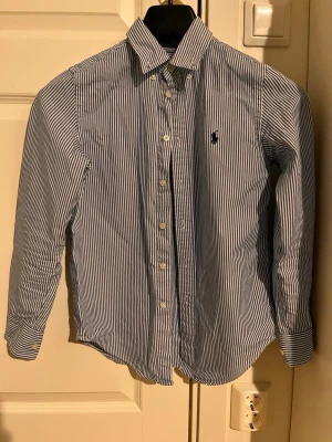 Blårandig skjorta från Ralph Lauren - Säljer denna Ralph lauren skjorta till ett off season pris. Den är givetvis äkta och kommer vara den perfekta skjortan att ha på stranden och kanske till och med stila för brudarna!