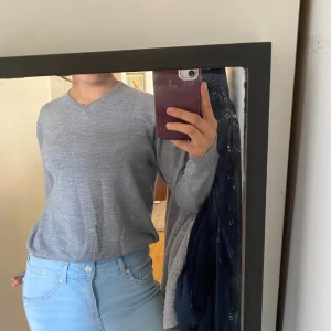 Grå v-ringad stickad tröja - Säljer en enkel och stilren grå stickad tröja med v-ringning. Tröjan har lång ärm och en normal passform, perfekt att matcha med jeans eller kjol. Mjuk och skön att bära under kyligare dagar.