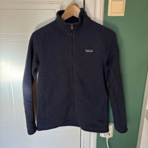 Mörkblå fleecejacka från Patagonia - En snygg mörkblå fleece från Patagonia med hel dragkedja och hög krage. Jackan har två fickor framtill och är tillverkad i mjukt fleecematerial. Den har inga skador eller defekter utan är bara lite nopprig som är lätt att få bort. Storleken är S men skulle även säga att den passar xs 