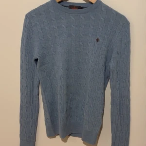 Ljusblå kabelstickad tröja Morris XS - Kabelstickad ljusblå tröja från Morris i 100% merinoull. Klassisk rund halsringning och diskret broderad logga på bröstet. Långärmad och perfekt för lager-på-lager under alla årstider. 