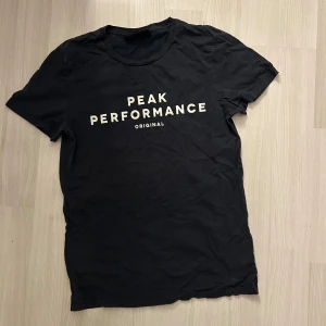 Mörkblå Peak Performance t-shirt - Mörkblå t-shirt från Peak Performance med vit logga tryckt på bröstet. Klassisk rund halsringning och korta ärmar. Tillverkad i mjuk bomull för en skön känsla. Perfekt för en clean och sportig look.