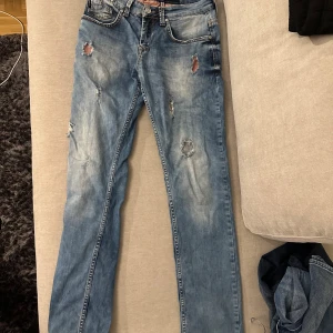 Blå jeans från Armani Jeans storlek W:30 L:34 - Snygga ljusblå jeans från Armani Jeans med slitna detaljer och hål på framsidan för en cool, avslappnad look. Klassisk femficksmodell med AJ-logga i metall på bakfickan och läderpatch i midjan. Passar dig som gillar streetstyle och vill sticka ut.