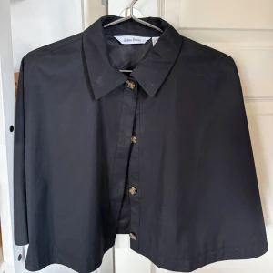 Svart poncho från & Other Stories - Cool svart poncho från & Other Stories med klassisk krage och knappar framtill. Modellen är loose och har en rak, lite boxig passform som ger en avslappnad vibe.