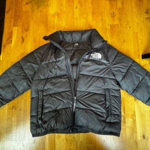 Svart pufferjacka från The North Face - Säljer en fin och varm The North Face-jacka i storlek XL som är nästan oanvänd och i mycket bra skick utan några hål eller skrapor. Den är perfekt för vintern då den både är riktigt varm och mysig, har en luva som smidigt kan fällas in bakom nacken med dragkedja samt stora rymliga fickor som rymmer mycket. En stilren och praktisk jacka för kalla dagar, för fler bilder eller frågor är det bara att höra av sig!
