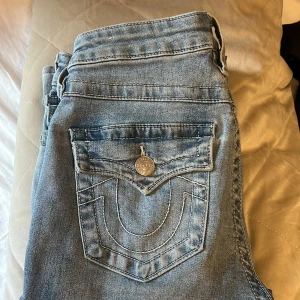 True Religion Becca Bootcut Jeans - Ljusblå jeans från True Religion, modell Becca Mid Rise Bootcut.Som nya fast endast lite slitning vid benen som man kan klippa bort och är inte så synligt när man går, köptes för ca 1200 på Johnells,säljs för 600,annars byte i modellen joey strlk 26