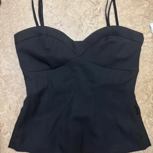 Svart korsett-topp med smala axelband - Snygg svart korsett liknande topp med smala axelband och markerad sweetheart-urringning. Från vila och storlek M, använd en gång. 