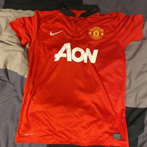 Manchester United Nike fotbollströja M - Klassisk Manchester United matchtröja från Nike med AON som sponsortryck. Röd med svart krage, klubbmärke på bröstet och Dri-FIT-material som andas. Perfekt för dig som vill visa ditt stöd på läktaren eller på planen.