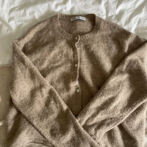 Beige stickad kofta från Zara XL - Mysig beige stickad kofta från Zara i storlek XL. Koftan har rund halsringning, knappar framtill och långa ärmar. Perfekt för lager-på-lager och chill höst- eller vinterstil.
