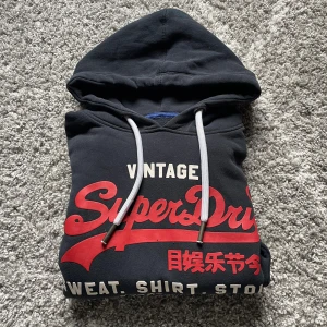 Superdry hoodie  - En svart superdry hoodie med rött tryck storlek L men passar också bra till M skriv gärna vid frågor eller minsta intresse:) typ nyskick