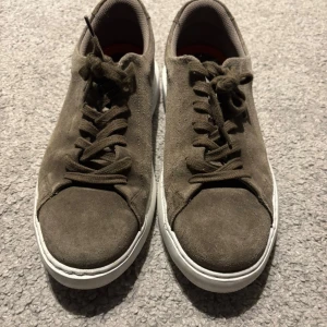 Bruna mockasneakers från Bianco - Snygga sneakers från Bianco i brun mocka med vita sulor. Skorna har klassisk rund tå, snörning och en stilren design som passar till det mesta. Insidan är fodrad i textil och sulan är platt för en bekväm känsla hela dagen.