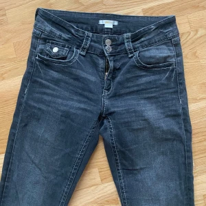 Mörkgrå bootcut jeans - Snygga mörkgrå jeans med boot vit  och klassiska fem fickor. Jeansen har kontrastsömmar, dubbla knappar i midjan och dragkedja. Perfekta för dig som gillar en enkel och stilren look.knappast andvänds