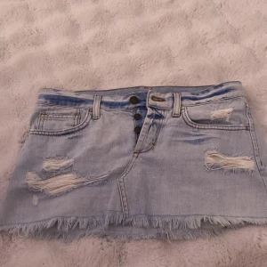 Ljusblå jeanskjol från Topshop - Säljer en ljusblå jeanskjol från Topshop i storlek 34. Har används 1 gång. Kjolen har slitna detaljer, fransig nederkant, knappar framtill och klassiska fickor både fram och bak. 