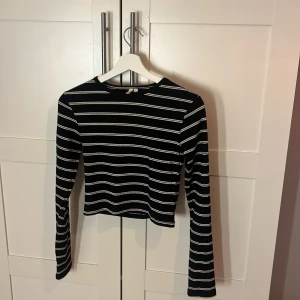 Svartvit randig croppad topp NLY Trend - Säljer en svart croppad topp från NLY Trend i storlek S. Toppen har vita horisontella ränder, lång ärm och är ribbad i materialet för extra struktur. Perfekt att styla med höga jeans eller kjol för en cool look.