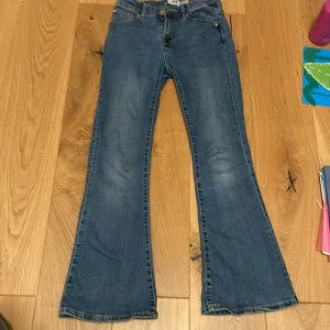 Blå Skippy Flare jeans från 157 - Snygga blå jeans från 157 med modellen Skippy Flare. De har klassisk femficksdesign, kontrastsömmar och en riktigt schysst bootcut med utsvängda ben. Jeansen är tillverkade i jeansmaterial och har en cool tvättad look.